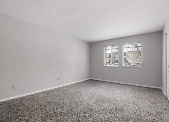 A room with grey carpet and two windows.