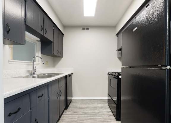 A black refrigerator is in a kitchen with a sink and cabinets.