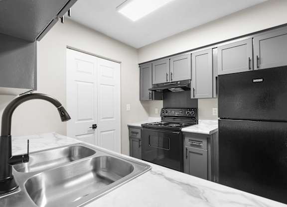 A kitchen with a black refrigerator, sink, and cabinets.