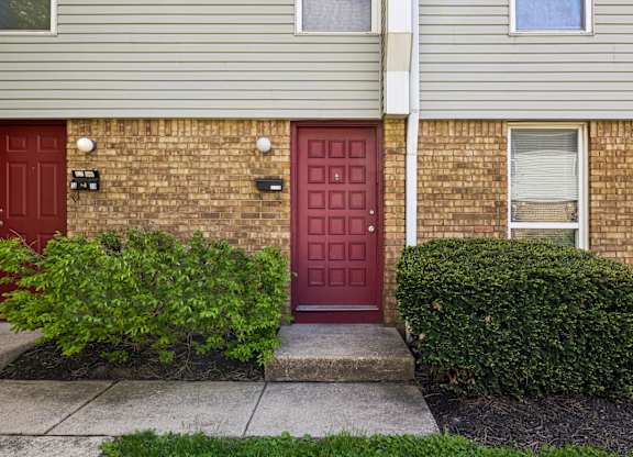 A red door is on the left side of a brick building. at Sharon Green Townhomes, Columbus, Ohio