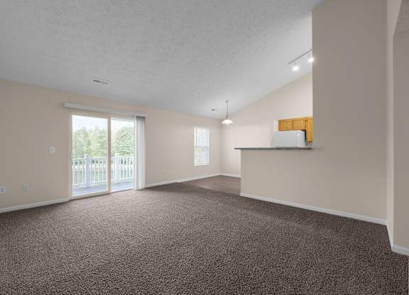A large, empty room with carpeted floor and a sliding glass door leading to a deck.