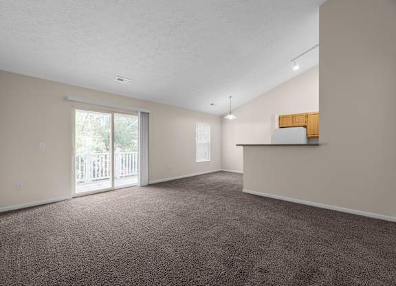 A spacious room with a carpeted floor and a sliding glass door leading to a balcony.