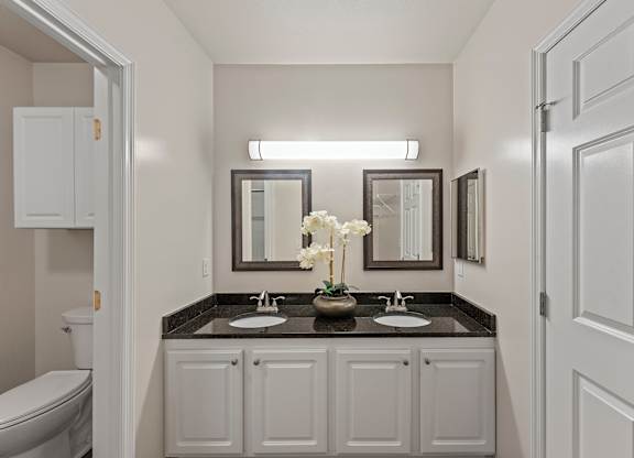 a bathroom with white cabinets and a black counter top with two sinks at Roebling Row, Covington, KY