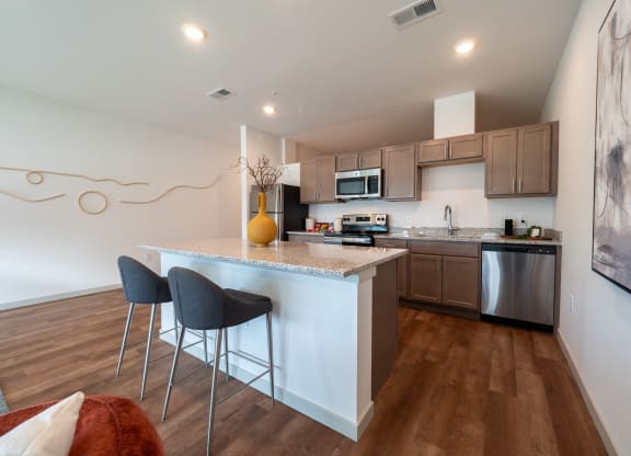 a kitchen with an island with two stools in front of it at The Row on Merchant Apartments, Springdale, OH