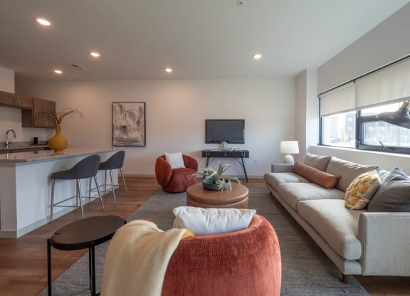 a living room with couches and chairs and a kitchen with a tv at The Row on Merchant Apartments, Springdale, 45246