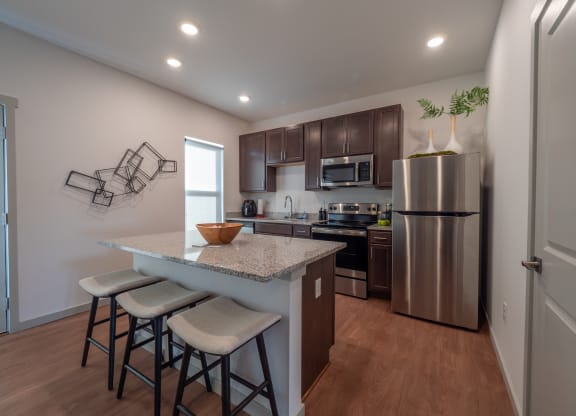 a kitchen with stainless steel appliances and a counter with three stools at The Row on Merchant Apartments, Springdale, Ohio