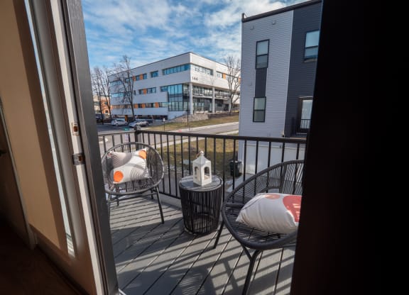 a balcony with chairs and a table and a view of a building at The Row on Merchant Apartments, Springdale, OH, 45246
