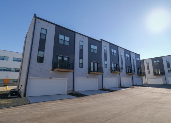 the exterior of a building with white and black siding and white garage doors at The Row on Merchant Apartments, Ohio