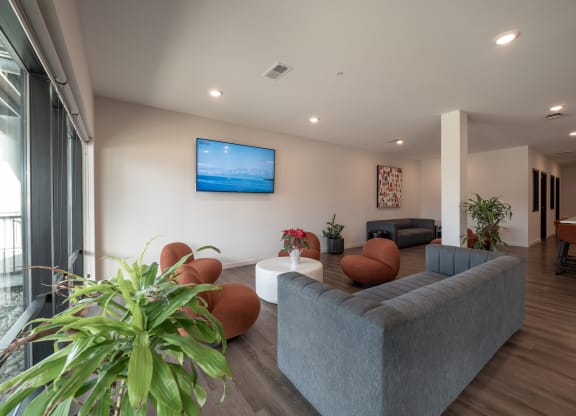 a living room with couches and chairs and a tv on the wall at The Row on Merchant Apartments, Springdale