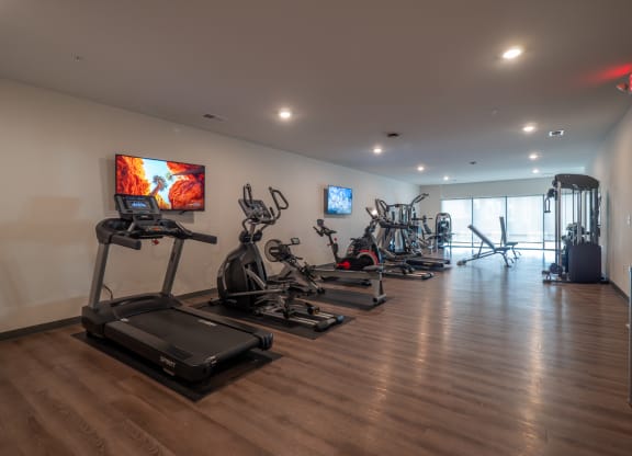 a gym with treadmills and other exercise equipment on a wooden floor at The Row on Merchant Apartments, Springdale, Ohio