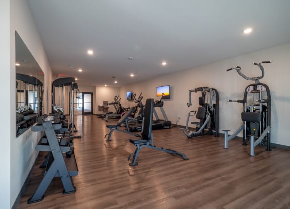 a gym with cardio equipment and weights on a wooden floor at The Row on Merchant Apartments, Springdale, 45246