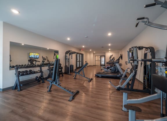 a gym with cardio equipment and weights on a wooden floor at The Row on Merchant Apartments, Springdale, OH