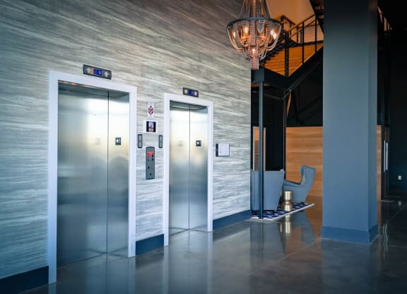 a lobby with three elevators and a chair and a chandelier