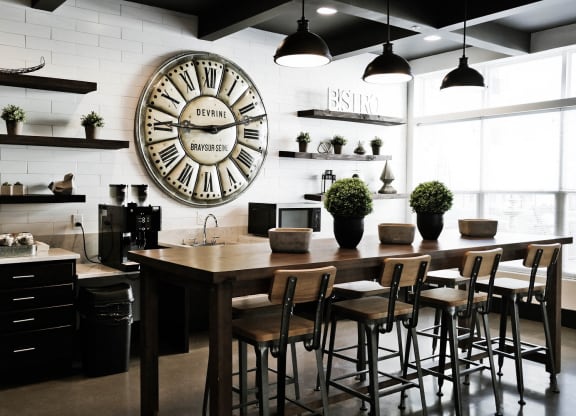 West Chester OH Apartments for Rent - Liberty Center - Community Coffee Bar with Rustic Design, Wooden Stool-Top Table with Chairs, Coffee Station, Storage Shelves, Tile Design, Large Clock, and light