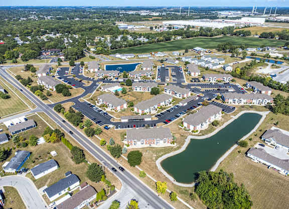 A bird's eye view of a residential area with houses, roads, and a pond.