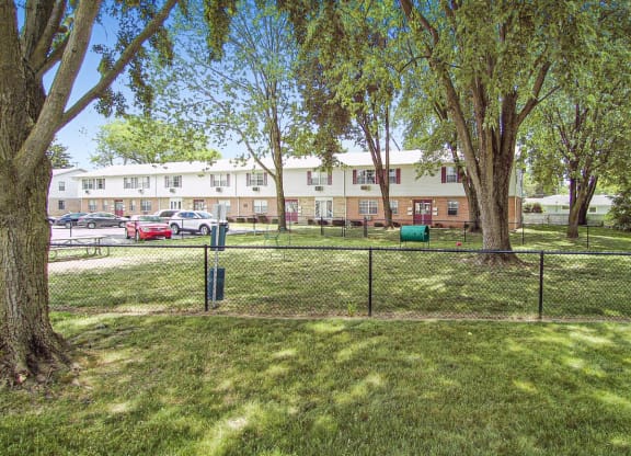 a fenced in dog park with trees and a building in the background