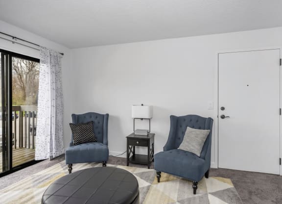 Living room with two blue chairs and a door to a balcony at Tall Timber Apartments, Cincinnati