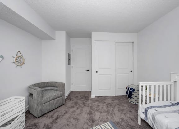 Bedroom with a crib and a chair and a closet at Tall Timber Apartments, Cincinnati