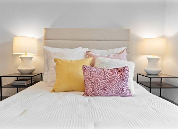 A bed with a white comforter and two pillows with a pink and yellow pillow.