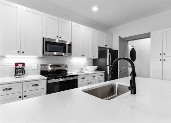 A modern kitchen with white cabinets and black appliances.