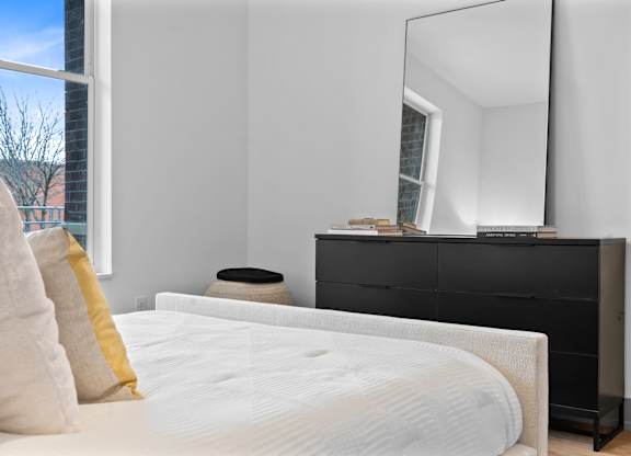 A bedroom with a white bed, a black dresser, and a large mirror.