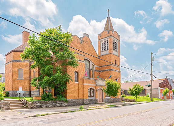 A church with a steeple and a cross on top is surrounded by a brick wall and trees. at The Ridge Apartments, Ohio