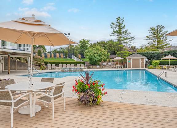 A poolside table with chairs and an umbrella overlooking a pool.