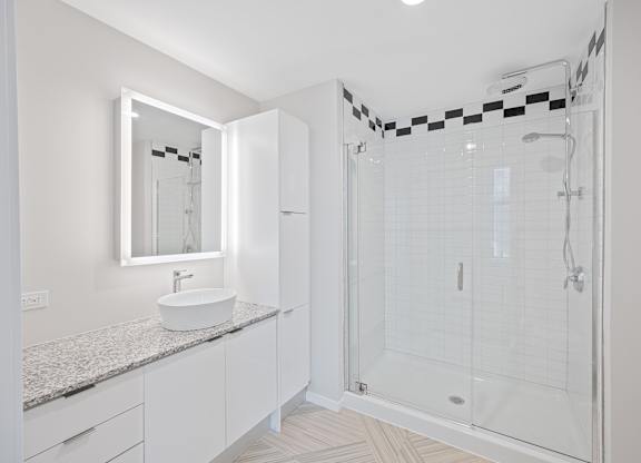 A white bathroom with a sink, mirror, and shower at Sky Central Apartments, Cincinnati, Ohio