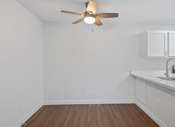 an empty living room with a ceiling fan and a kitchen