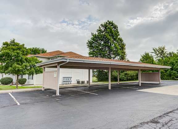 a covered parking lot with a white building and trees