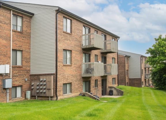 a brick apartment building with balconies and a green yard at The Woodridge Collection, Fairfield, OH 45014