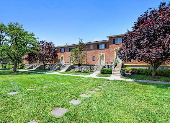 a large brick building with stairs and grass and trees at Gainsborough Court Apartments, Fairfax, Virginia