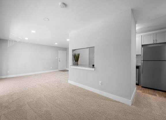 a living room with white walls and carpet and a black refrigerator at Gainsborough Court Apartments, Fairfax, VA, 22030