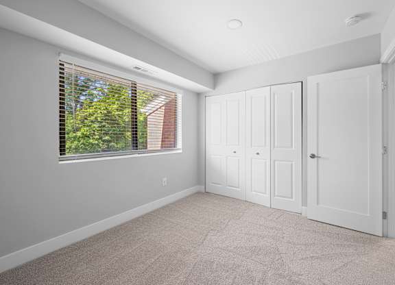 an empty bedroom with a large window and white doors at Gainsborough Court Apartments, Virginia