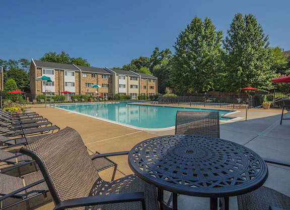Outdoor table seating area with lounge chairs by the pool at Tysons Glen Apartments and Townhomes, Falls Church