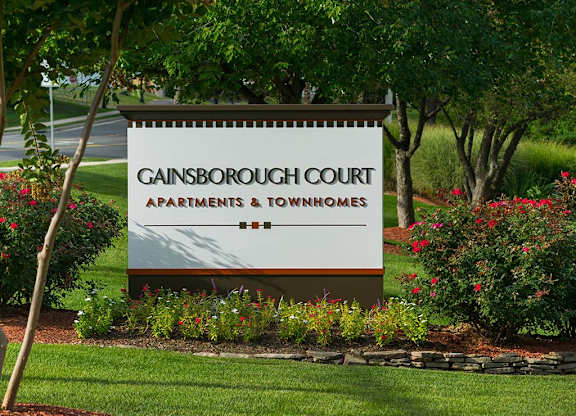 A sign for Gainsborough Court Apartments & Townhomes is surrounded by flowers and trees at Gainsborough Court Apartments, Fairfax, 22030