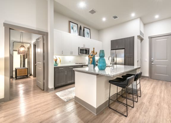 An Open Kitchen With A Large Island With Bar Stools at The Bridge at McKinney, McKinney, Texas, 75069