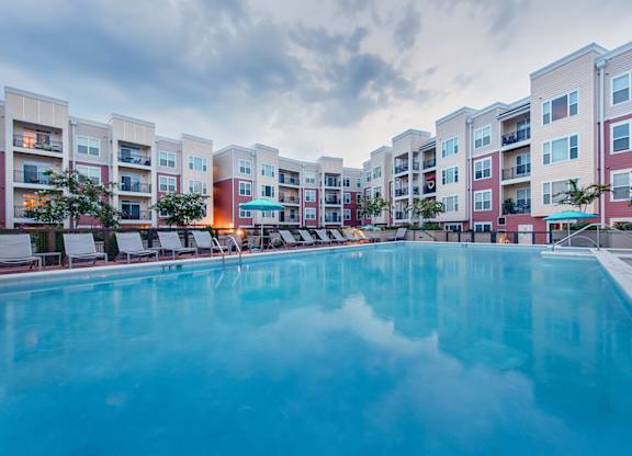 a swimming pool with lounge chairs and umbrellas in front of an apartment building