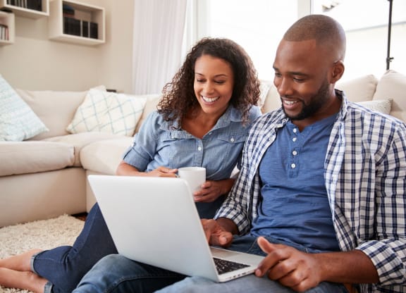 a man and woman sitting on the floor using a laptop computer