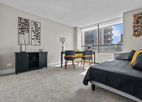 A bedroom with a black bed, a grey carpet, and a black cabinet with a plant on top.