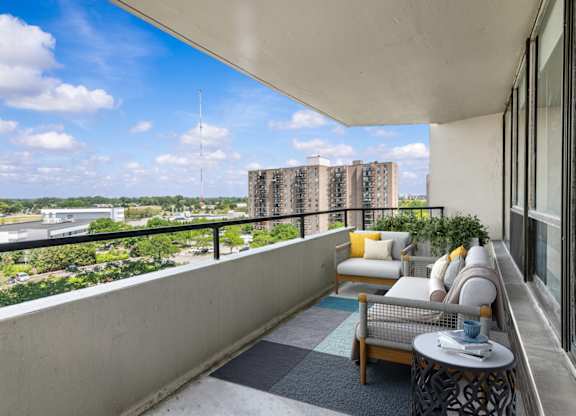 A balcony with a couch, chairs, and a table overlooking a cityscape.