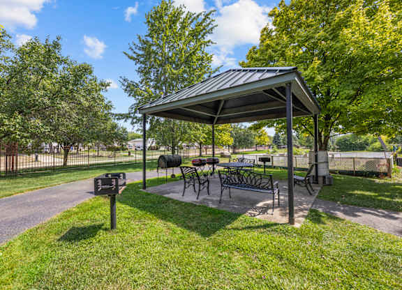 A covered picnic area with tables and chairs is surrounded by trees.