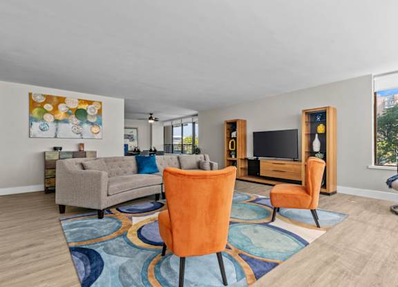A living room with a grey couch, orange chairs and a painting on the wall.