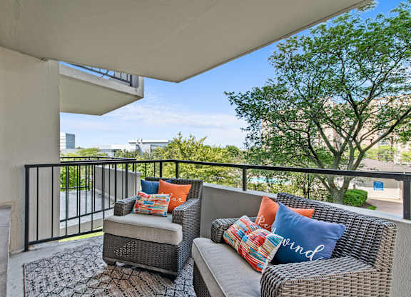 A balcony with a couch and pillows overlooking a parking lot.