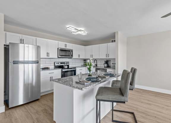 A modern kitchen with a stainless steel refrigerator and a marble island.