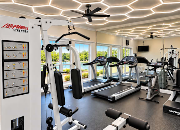 A gym with a variety of equipment including treadmills, weights, and a ceiling fan.