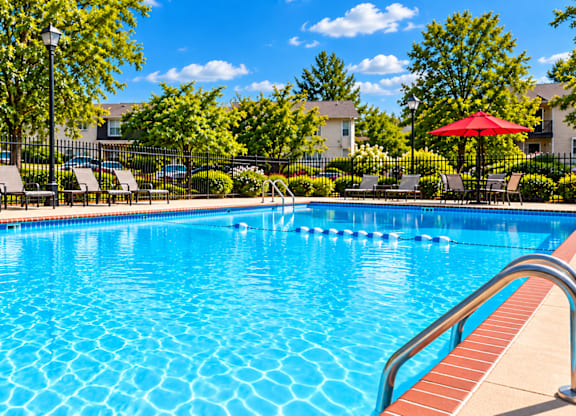 A swimming pool surrounded by trees and chairs.