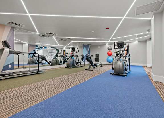 A gym with a blue mat in the foreground and various exercise equipment.