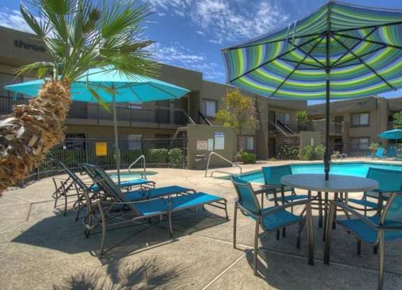 A poolside area with a table, chairs, and umbrellas.