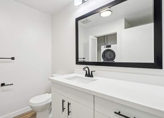 A bathroom with a white countertop and a mirror reflecting a fan.